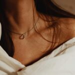 Close-up of a woman's collarbone with a necklace and tattoo, wrapped in fabric.